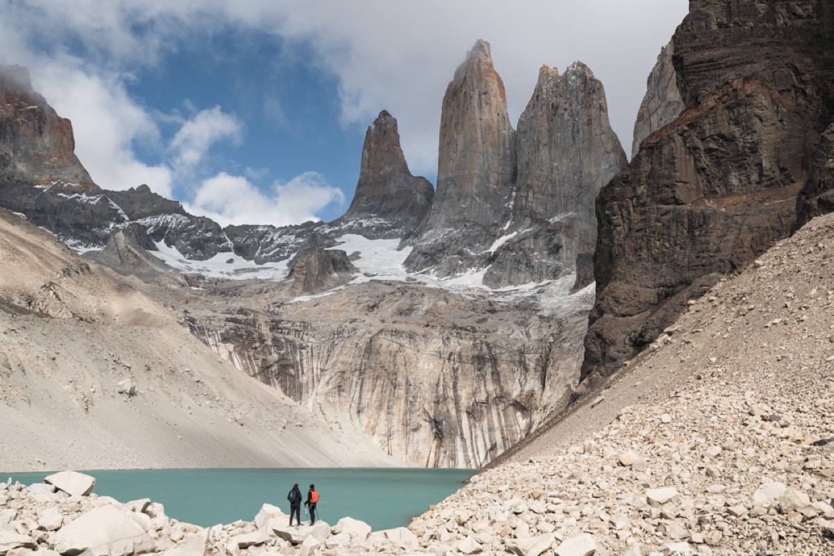Two hikers at the glacial lagoon below the three granite towers of Torres del Paine