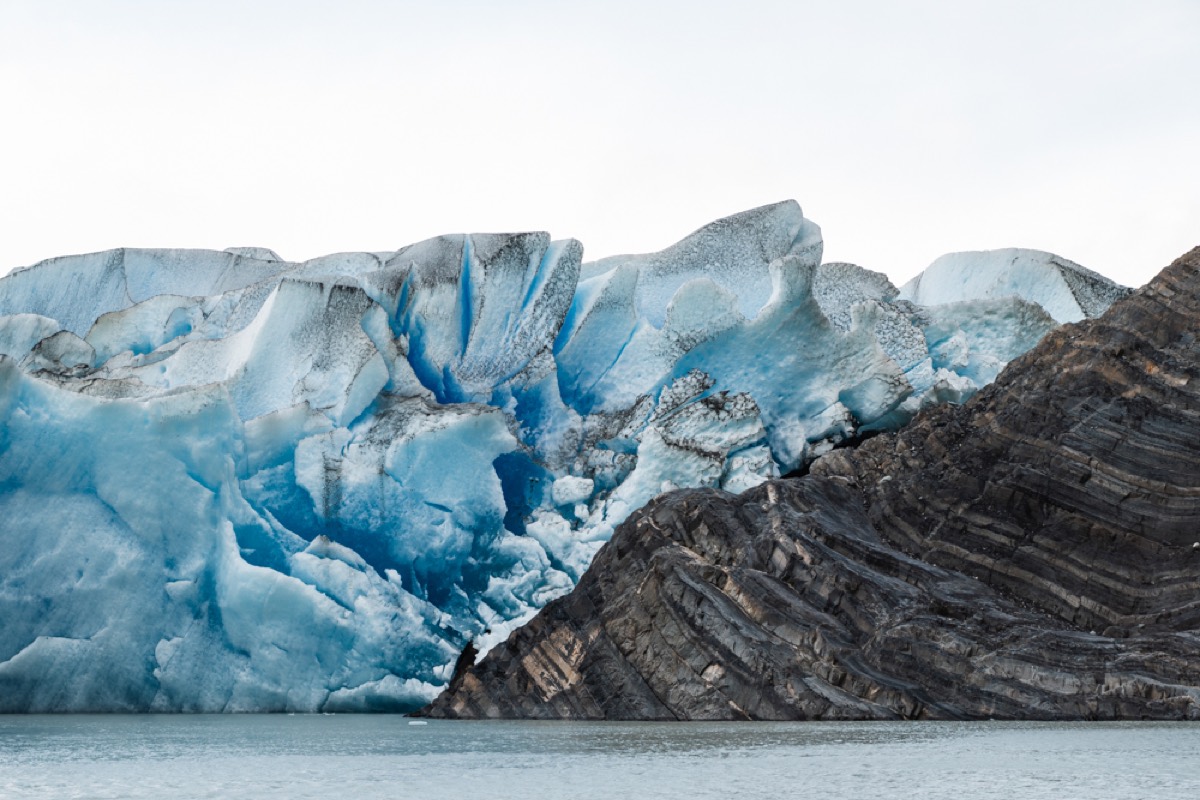 The blue ice wall of Grey Glacier meeting a rocky ridge, seen from the water