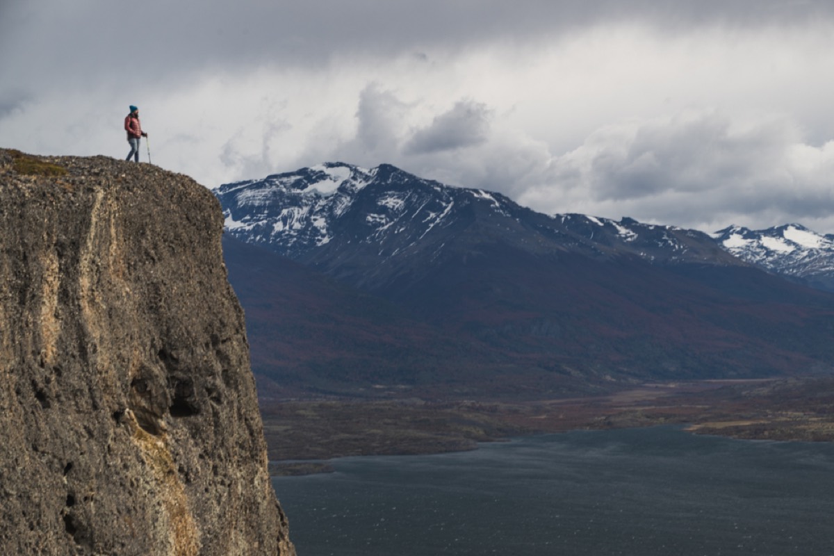 A lone hiker on a cliff edge above the valley and fjord near Puerto Natales