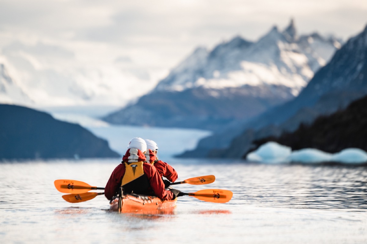 Two people kayaking on calm water toward snow-capped Patagonian peaks