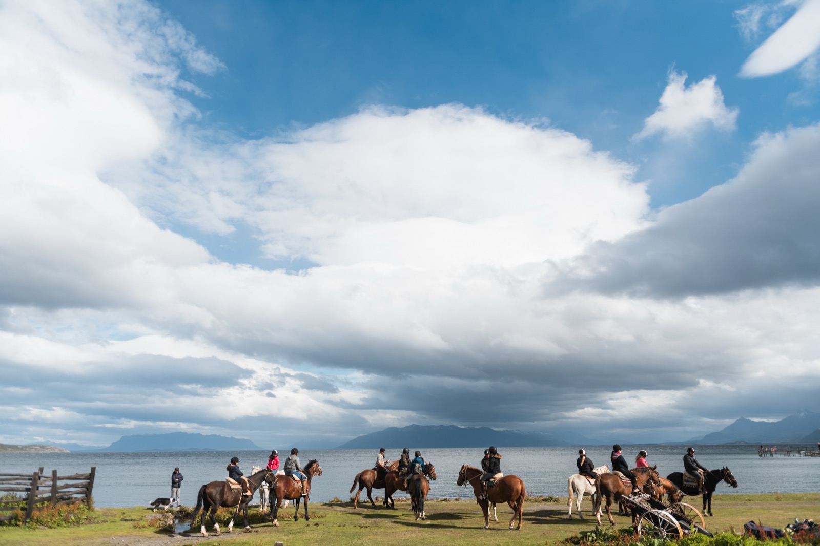 Two riders on horseback crossing the golden Patagonian steppe by a lake, snow-dusted mountains behind