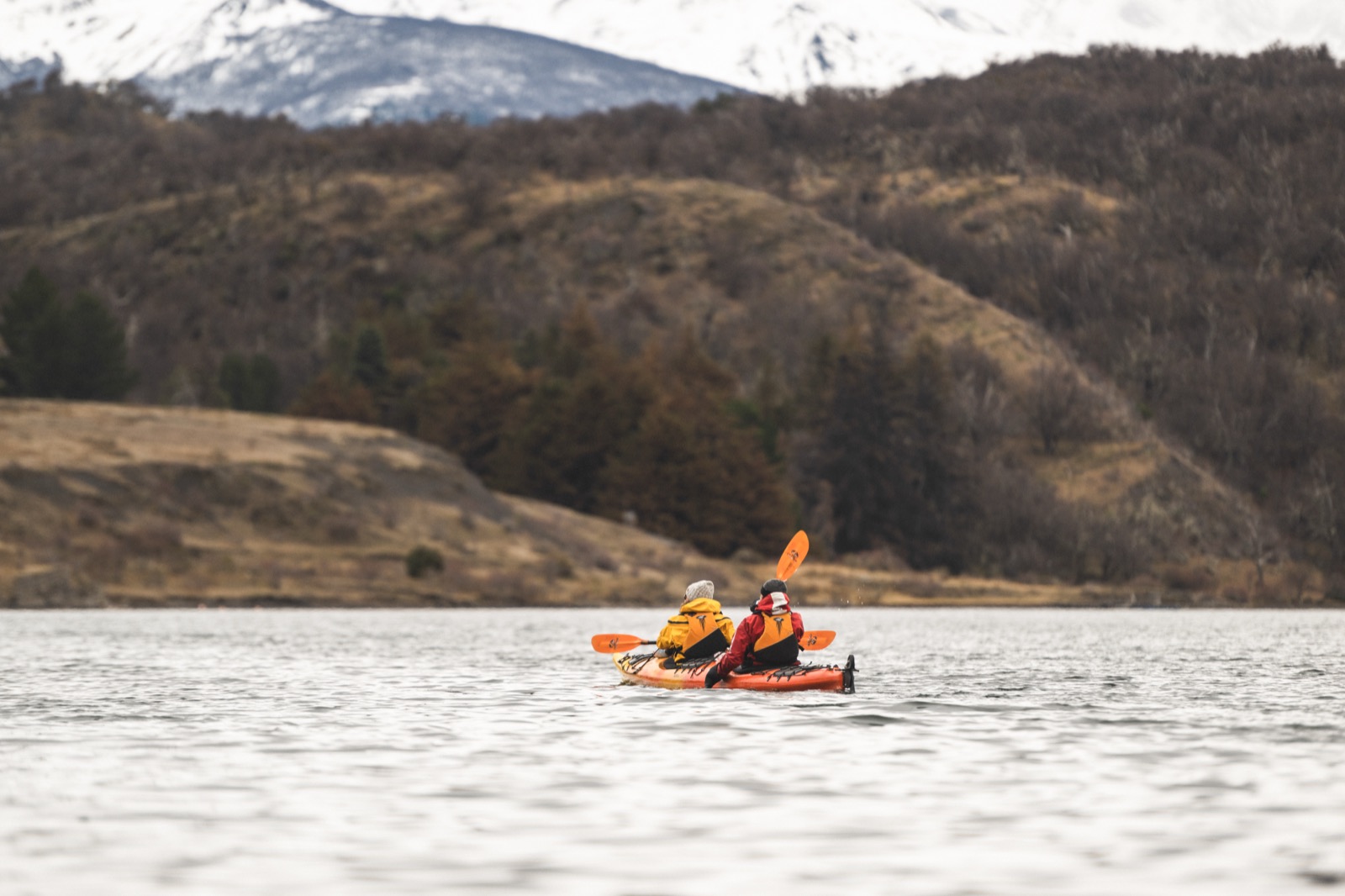 Two people kayaking on calm water toward snow-capped Patagonian peaks