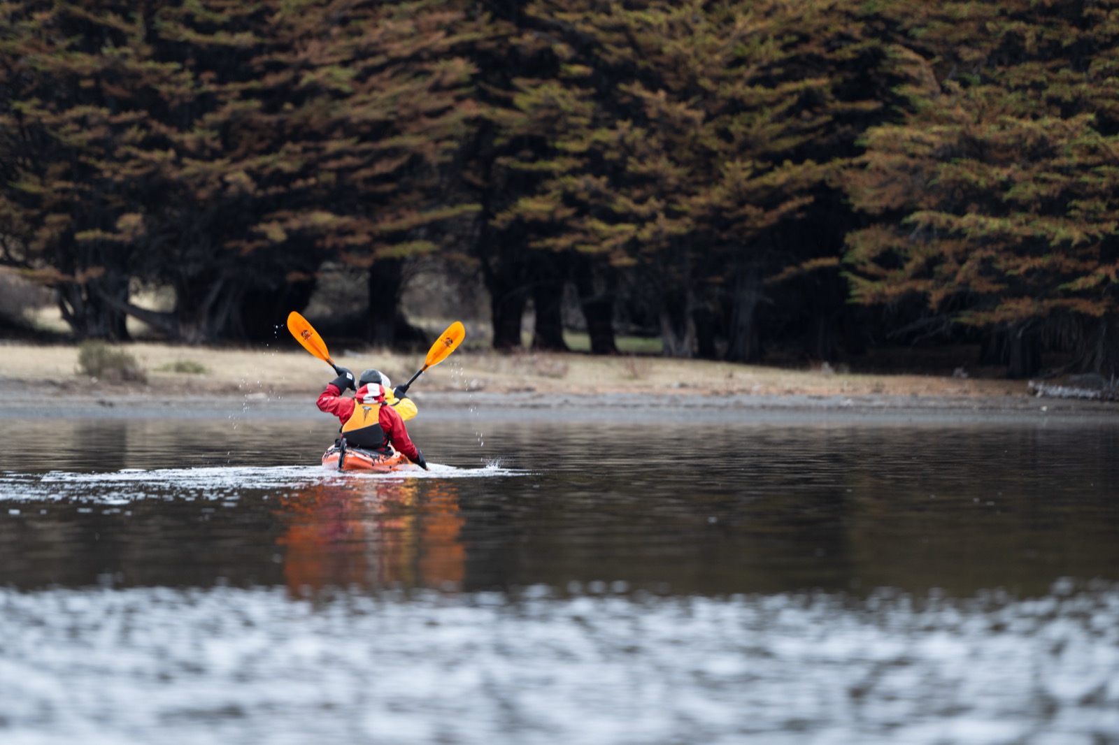 Two people kayaking on calm water toward snow-capped Patagonian peaks