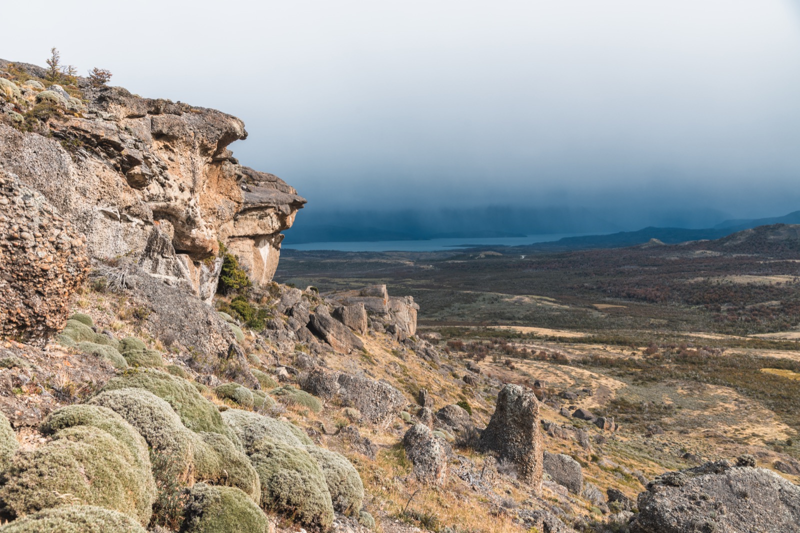 A lone hiker on a cliff edge above the valley and fjord near Puerto Natales