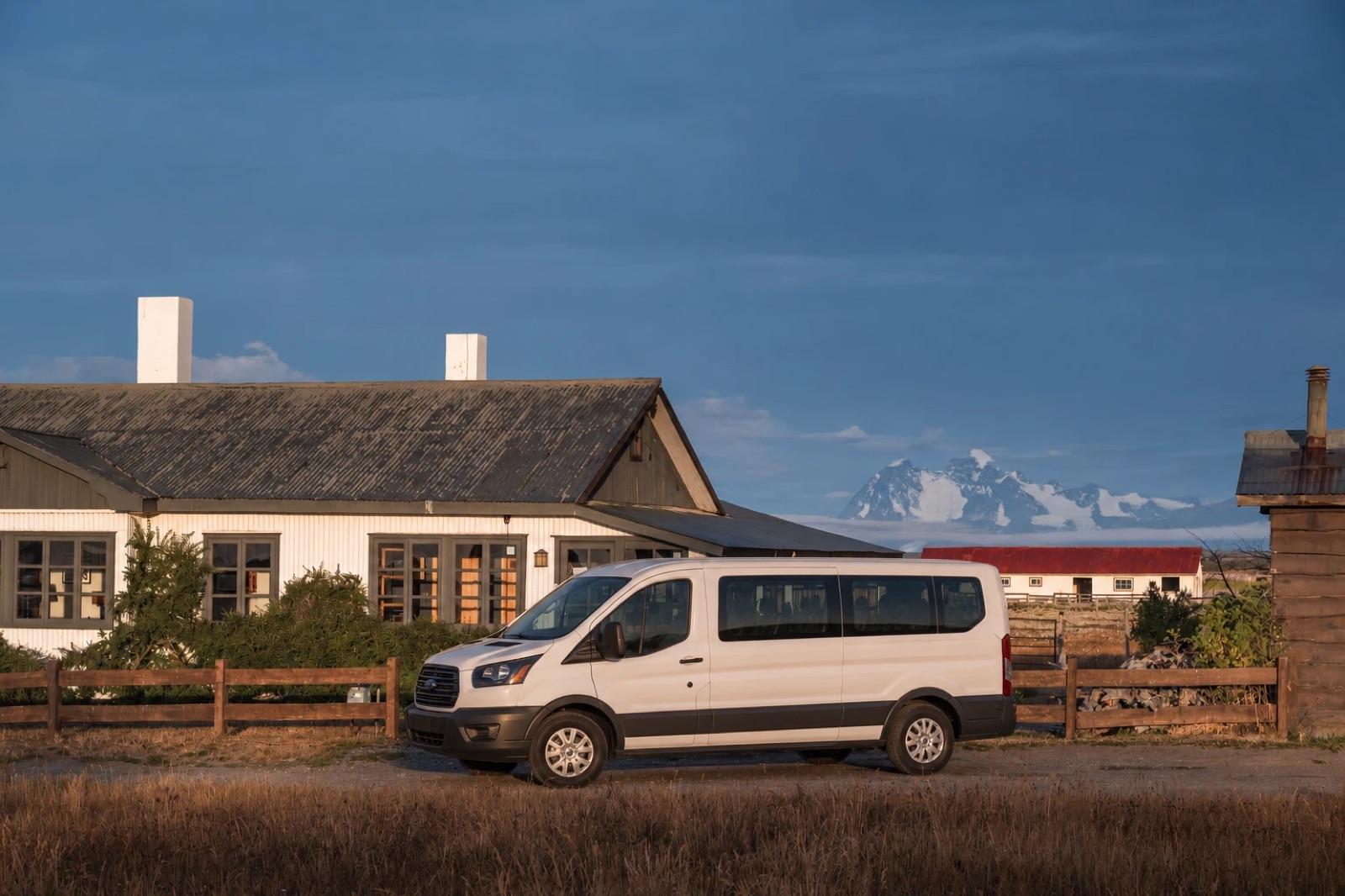 A white passenger van parked in front of Bories, with snowy mountains behind